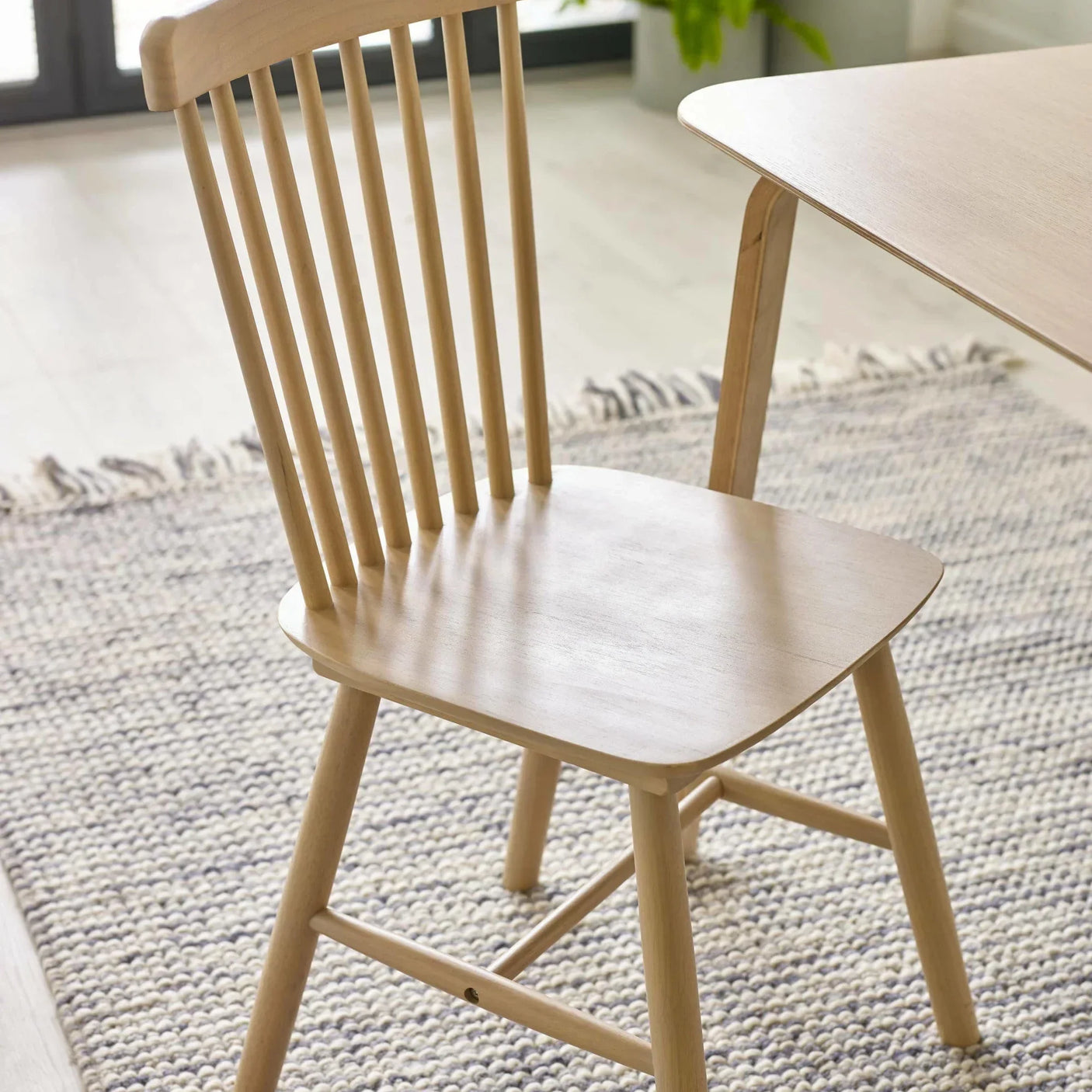 Light oak wooden dining chair with spindle back next to matching table on textured rug