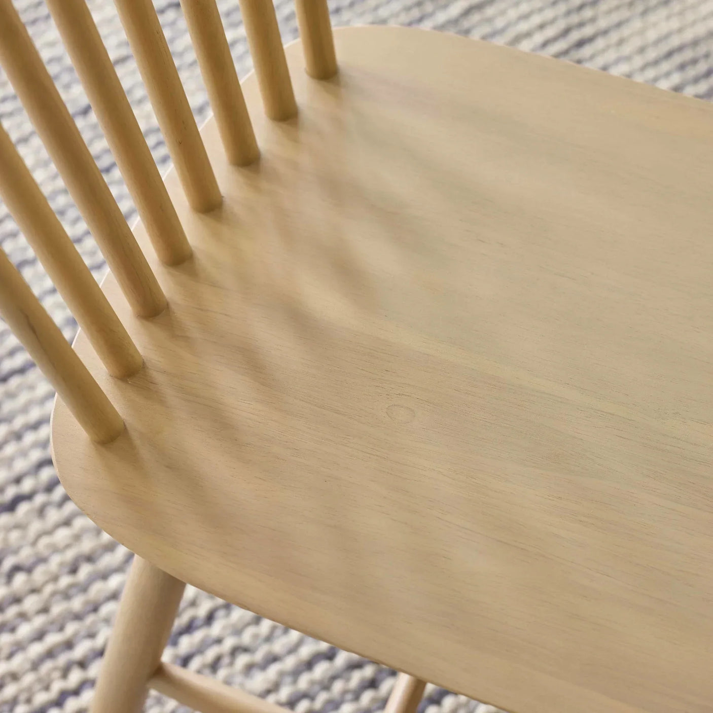 Closeup of natural wood dining chair seat and spindle back on patterned rug