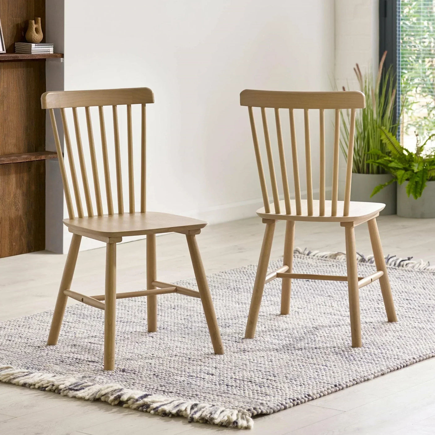Pair of wooden dining chairs with spindle backs on woven rug in modern dining room