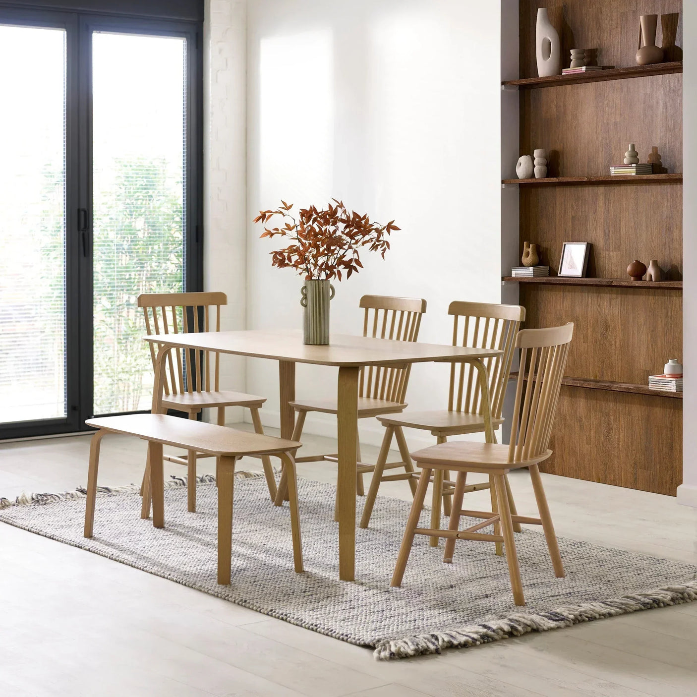 Light oak dining table set with four chairs and bench on a woven rug in modern dining room