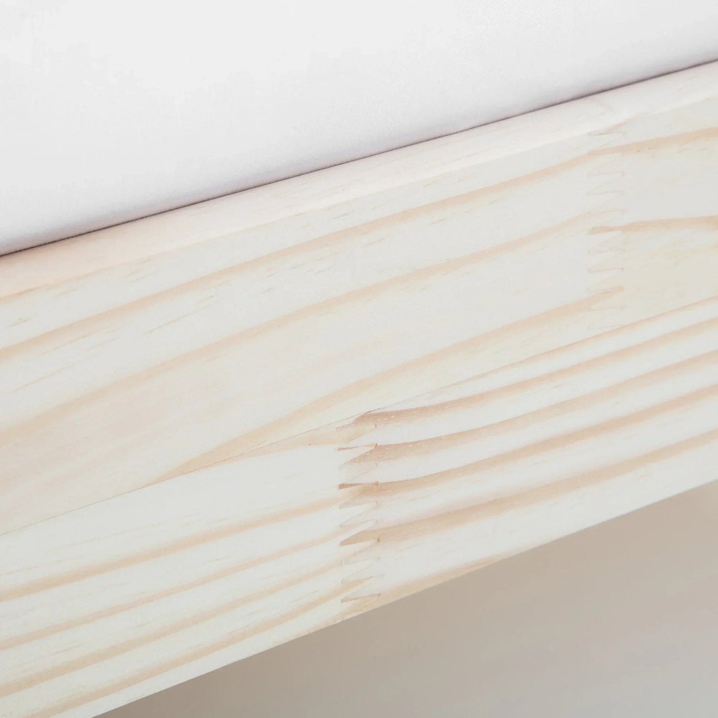 Close-up of light wood bed frame corner with visible grain and joint detail