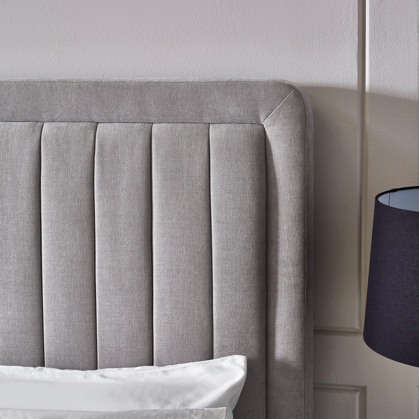 Upholstered grey bed headboard with vertical panels and white bedding