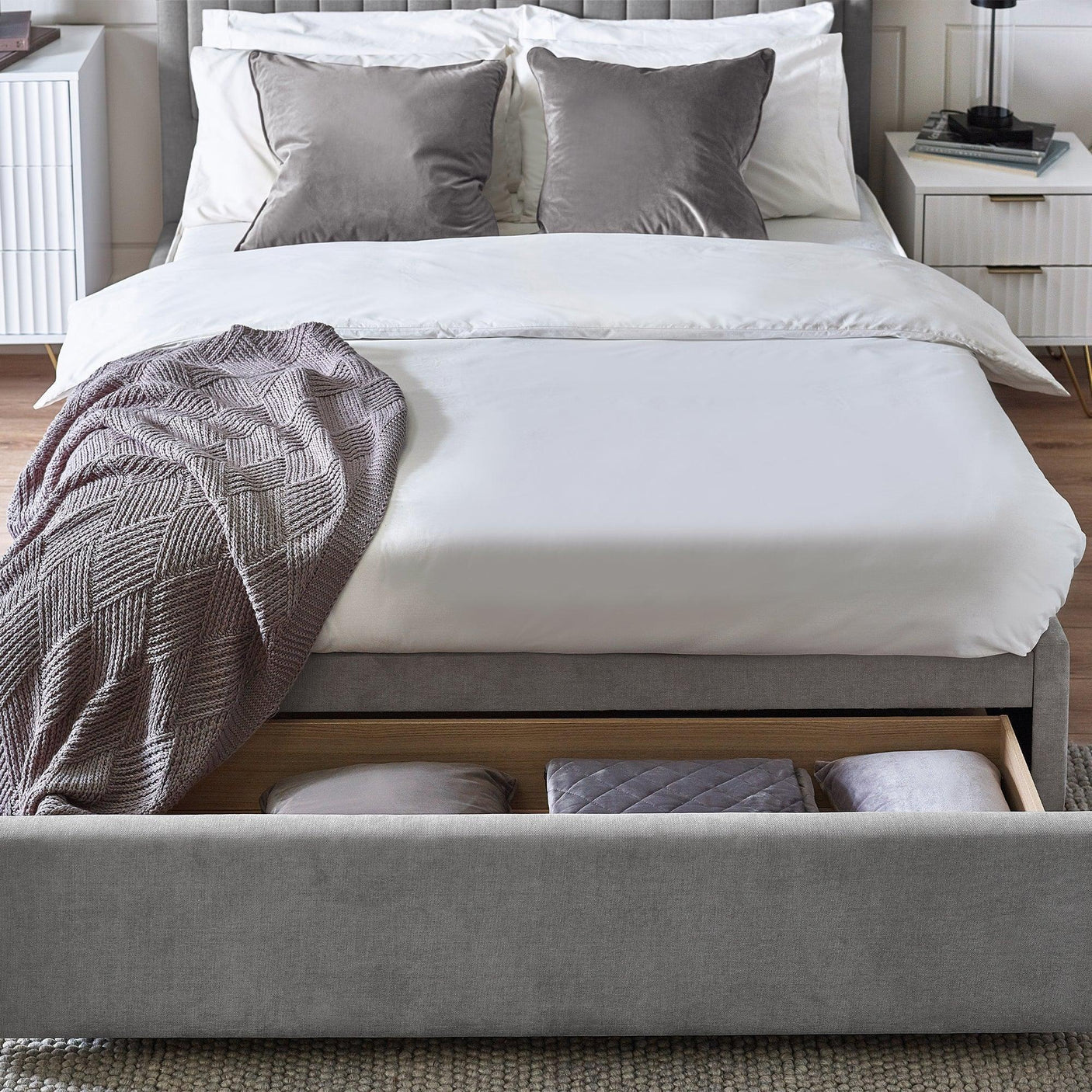 Grey upholstered bed with storage drawer open, pillows and throw blanket in modern bedroom