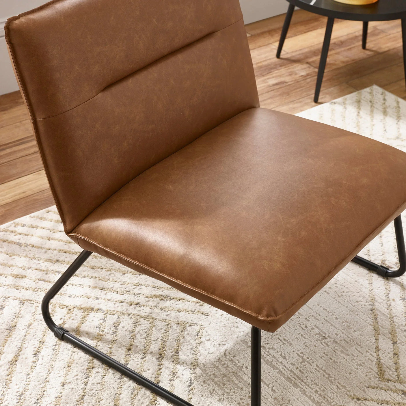 Brown leather accent chair with black metal legs on textured cream rug