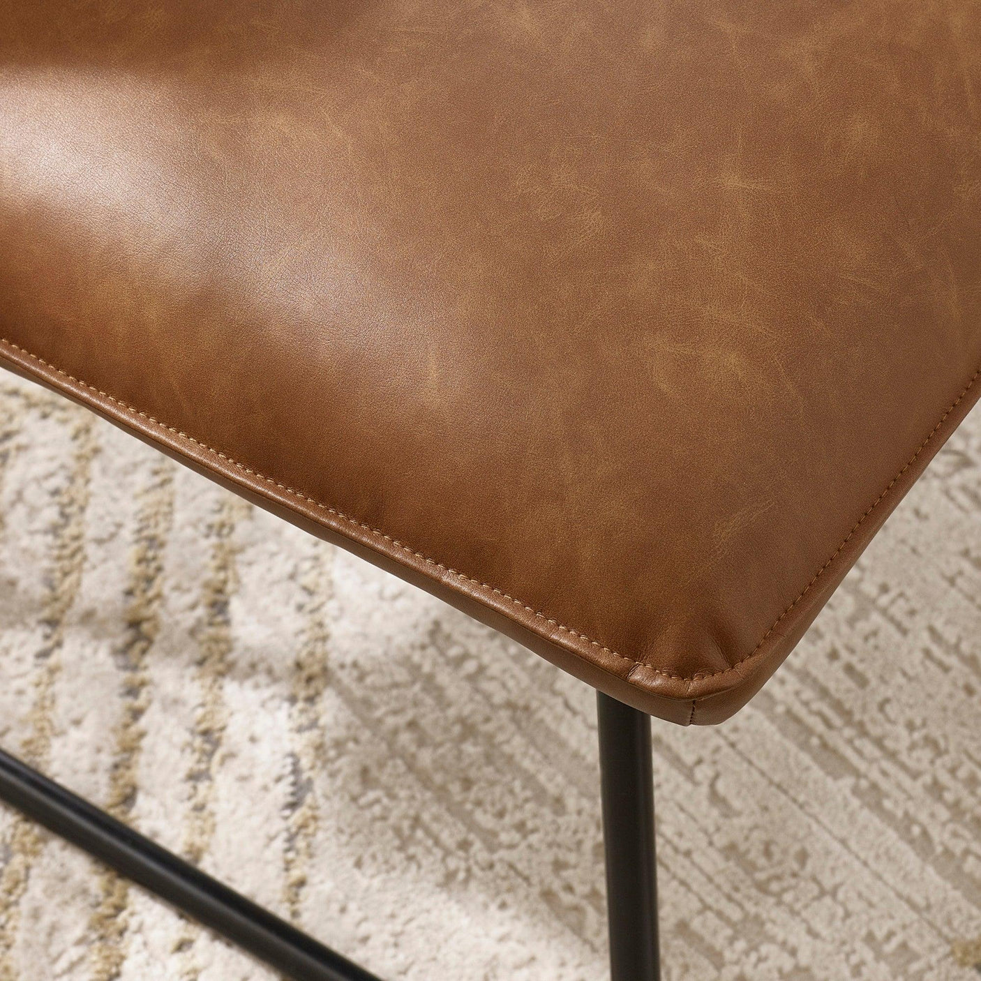 Closeup of brown leather dining chair seat with black metal legs on patterned rug