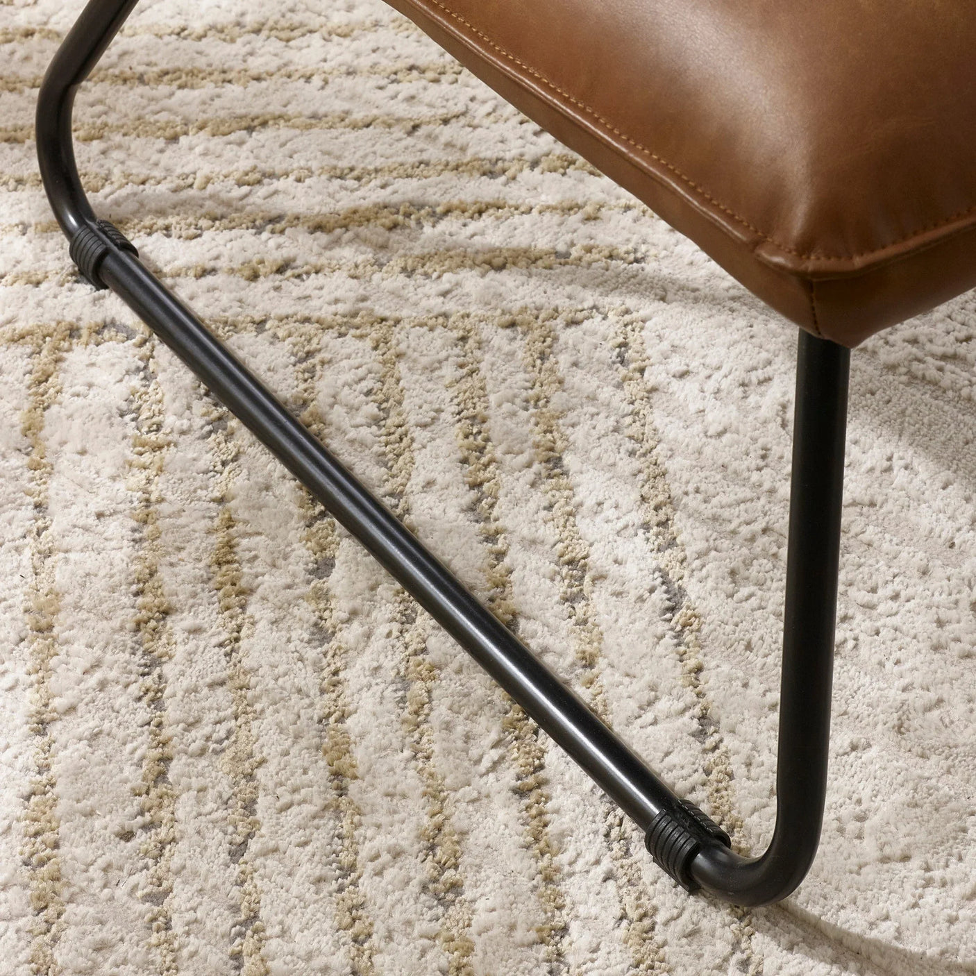 Close view of brown leather chair seat and black metal frame on textured beige rug