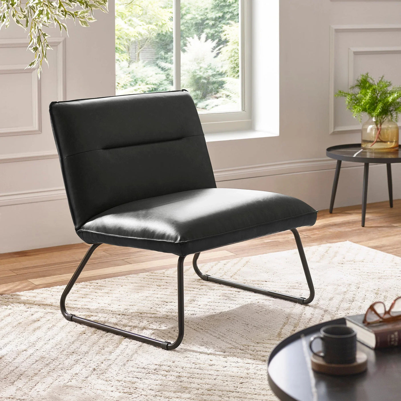 Black leather accent chair with metal legs in modern living room setting near window