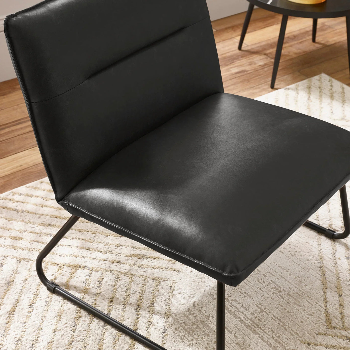 Black faux leather accent chair with metal frame on cream patterned rug