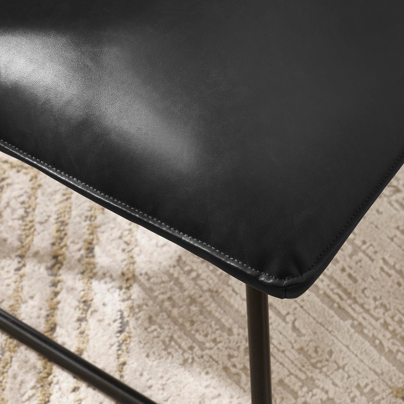 Close-up of black faux leather dining chair seat with stitched edge and metal legs