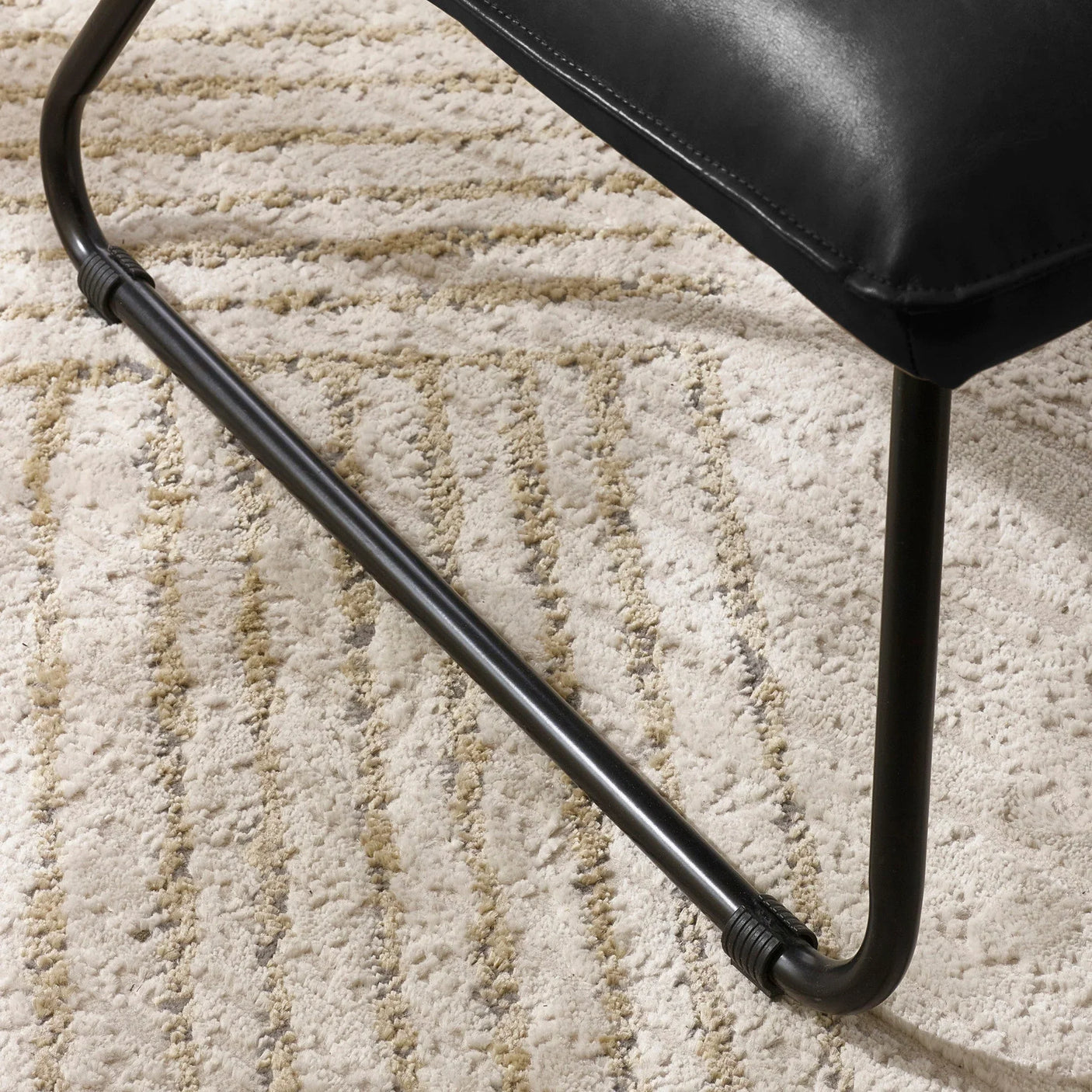Black metal chair leg with cushioned seat on cream textured rug