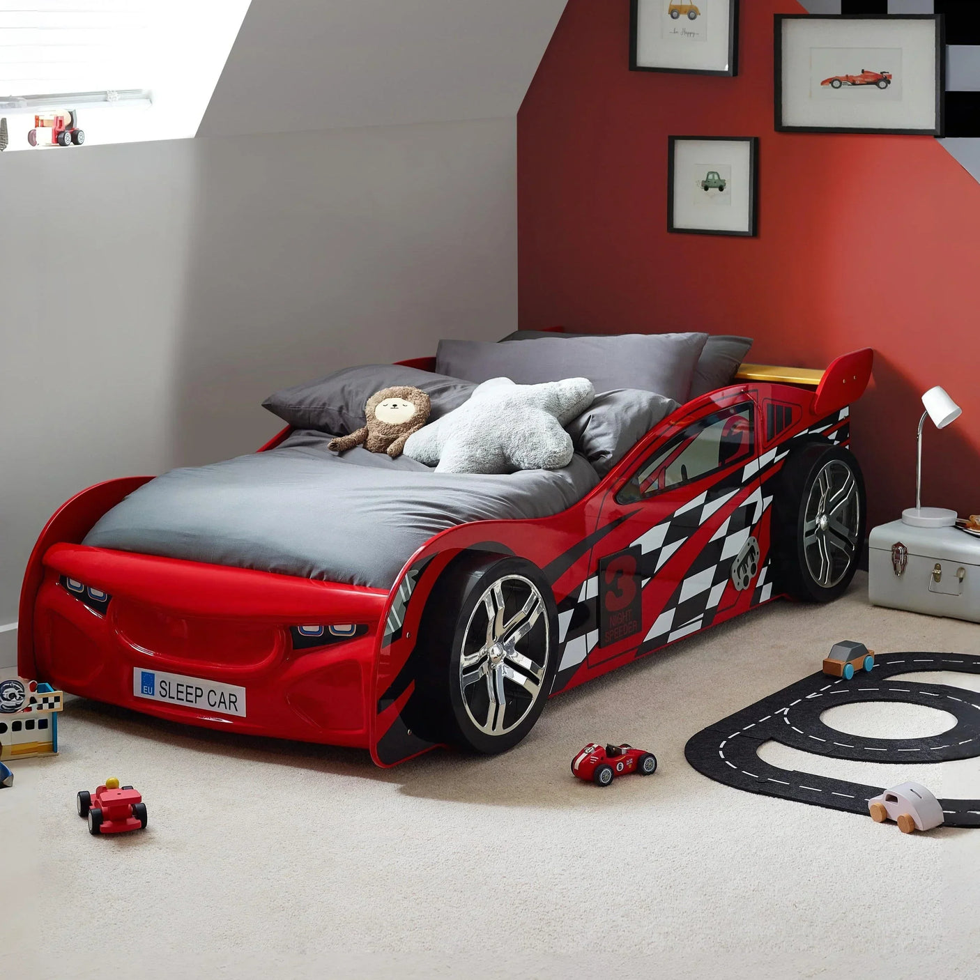 Red race car bed for kids with checkered sides in themed bedroom with wall art and toys