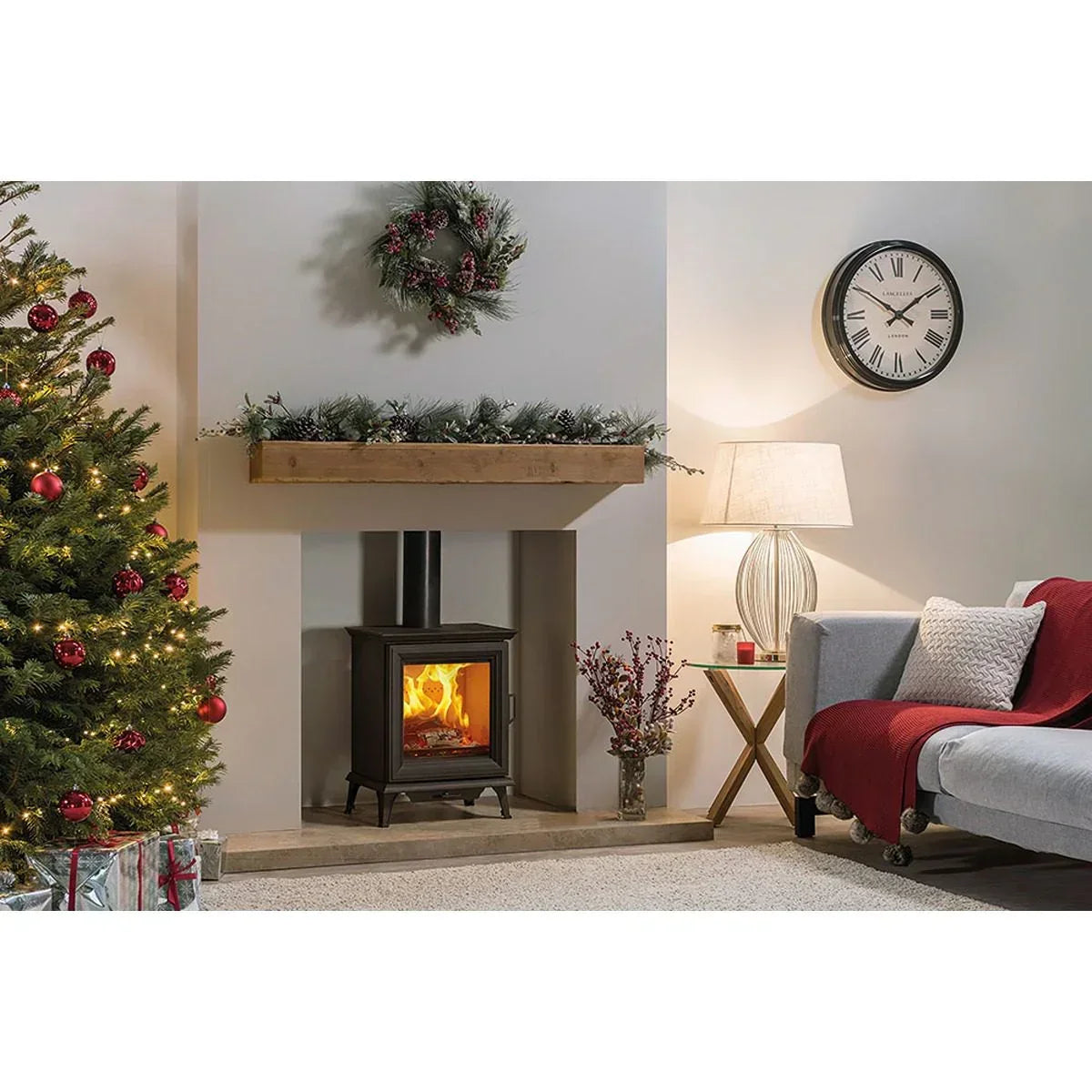Living room with wood burning stove, Christmas tree, grey sofa, and festive decorations