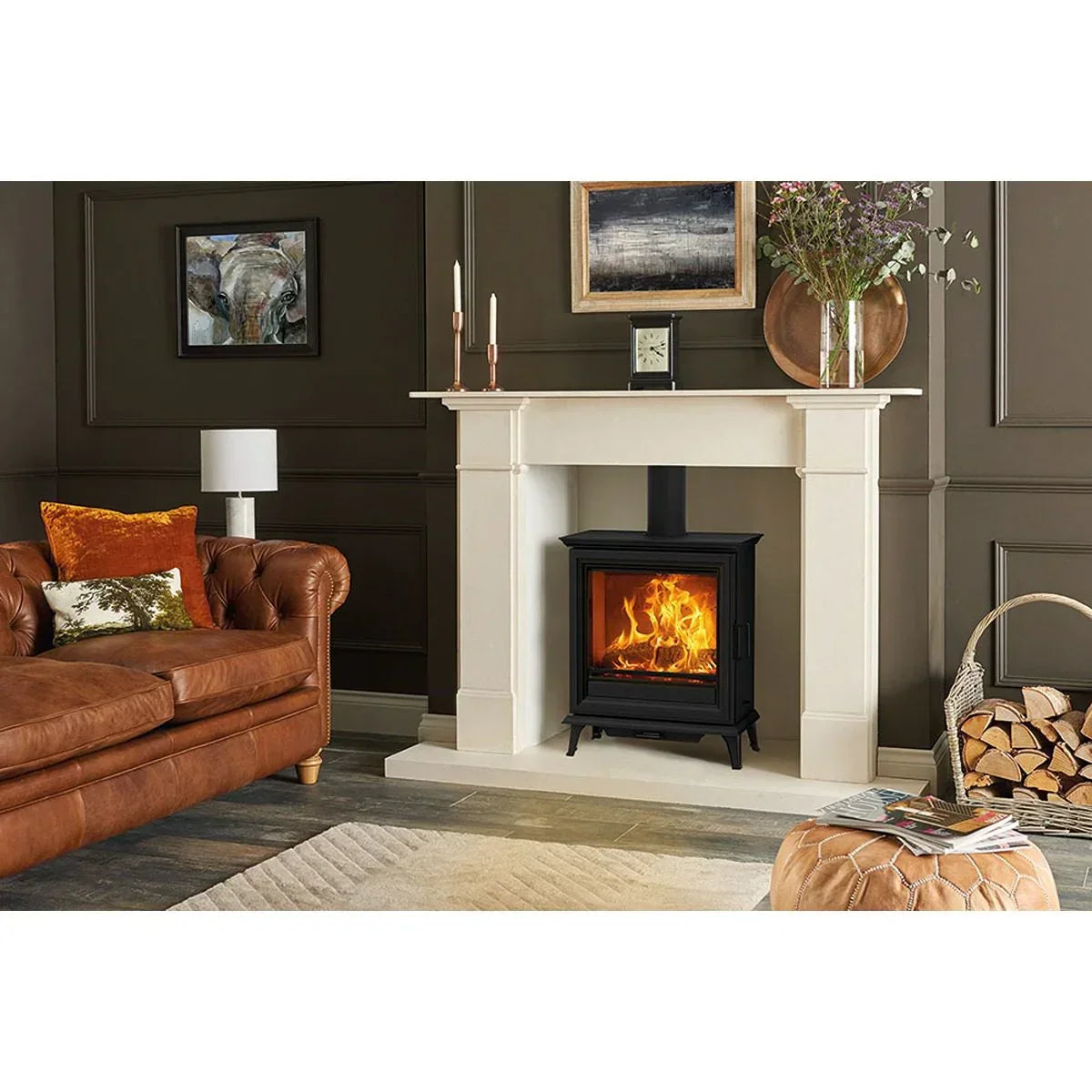 Black wood burning stove in cream fireplace with brown leather sofa and log basket