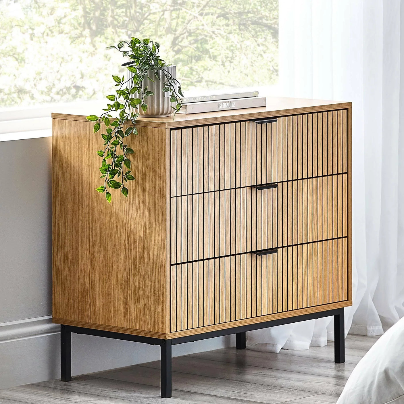 Wooden 3 drawer chest with vertical slat design, black legs, potted plant on top