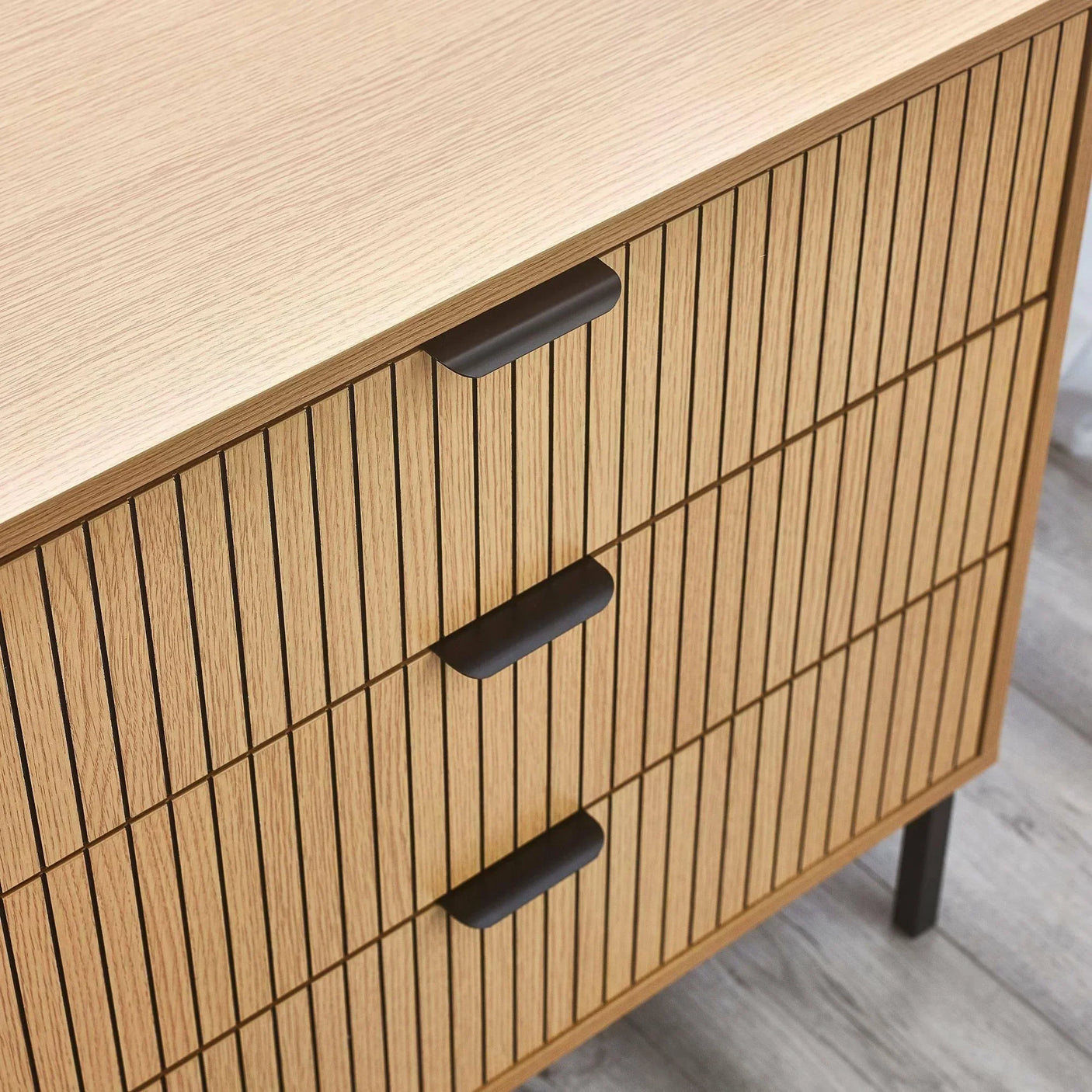 Oak wood chest of drawers with slatted front and black handles on grey wooden floor