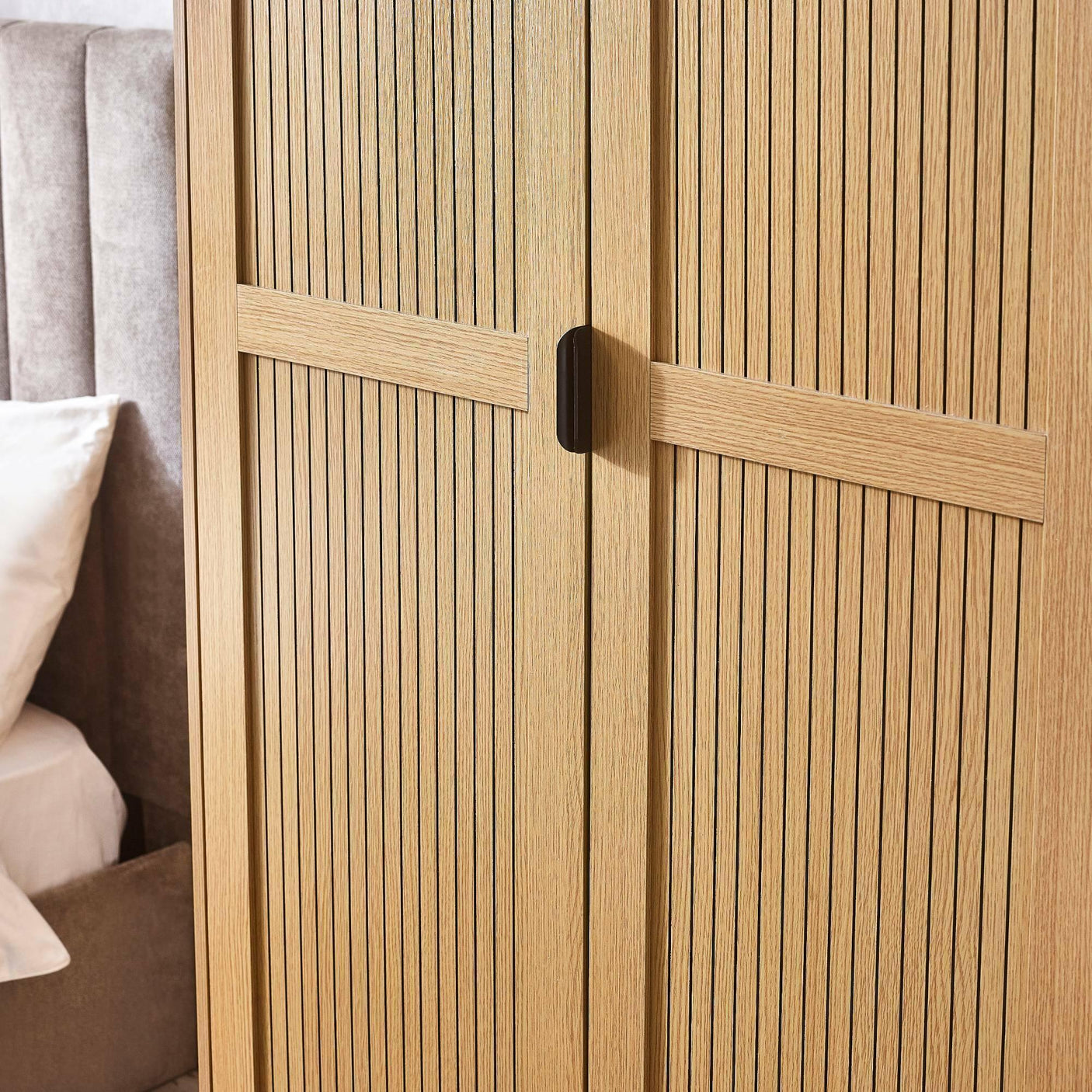 Oak wood wardrobe with vertical slatted doors beside upholstered grey bed