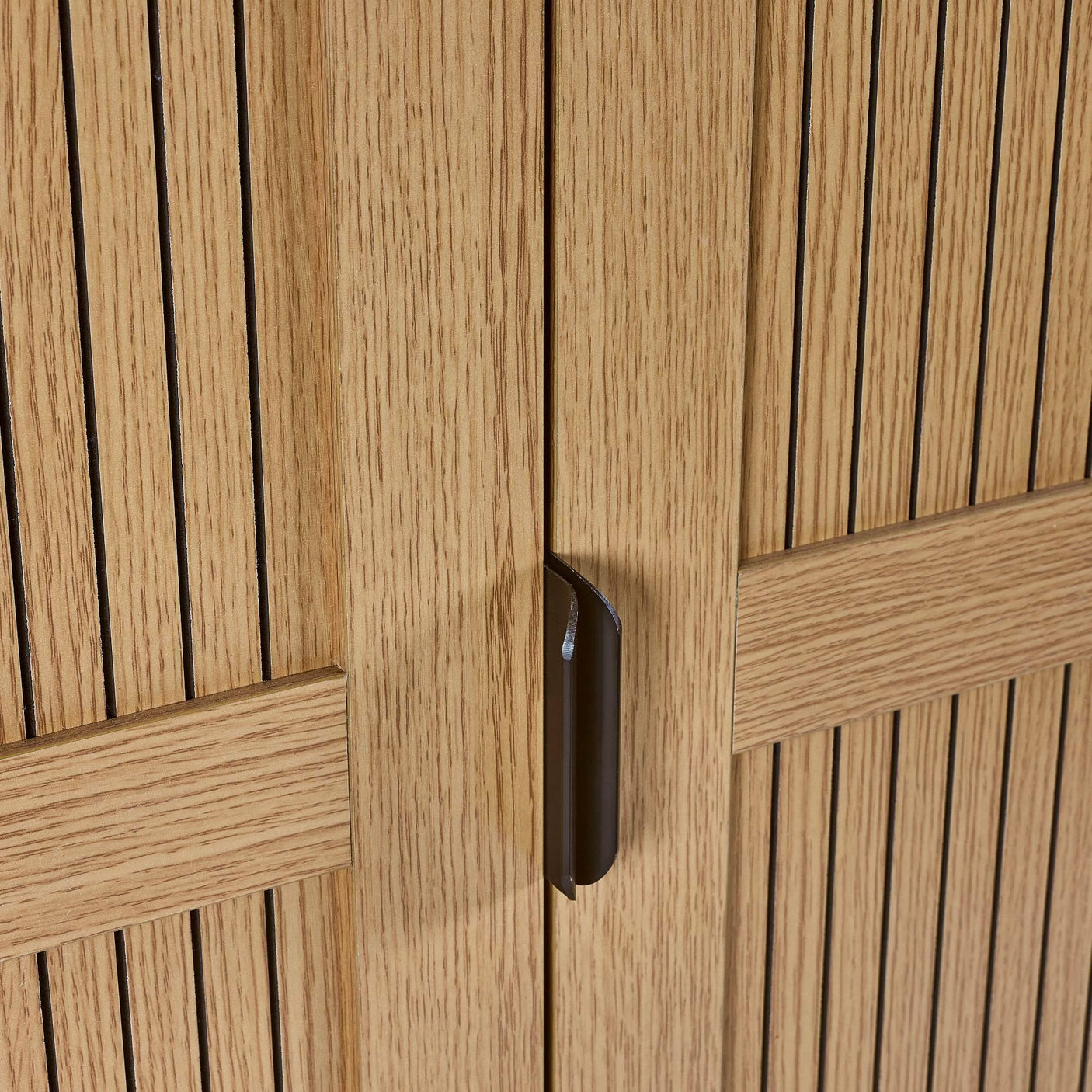 Close up of wooden cabinet doors with vertical grooves and black metal handle