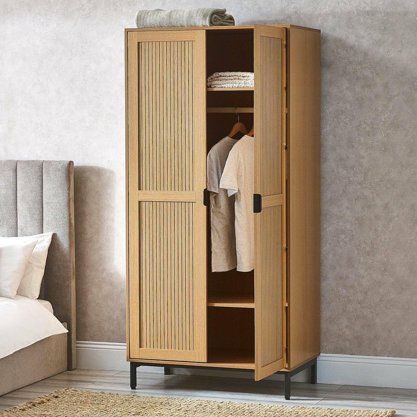 Oak wardrobe with vertical grooves, open doors, hanging rail and shelves in bedroom