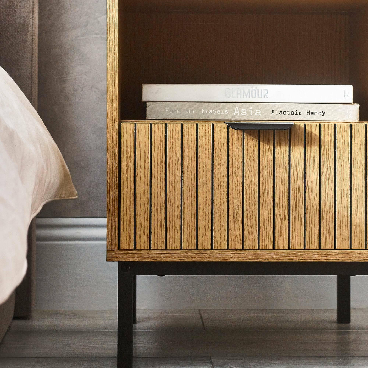 Slatted oak bedside table with black legs beside bed, two books on open shelf