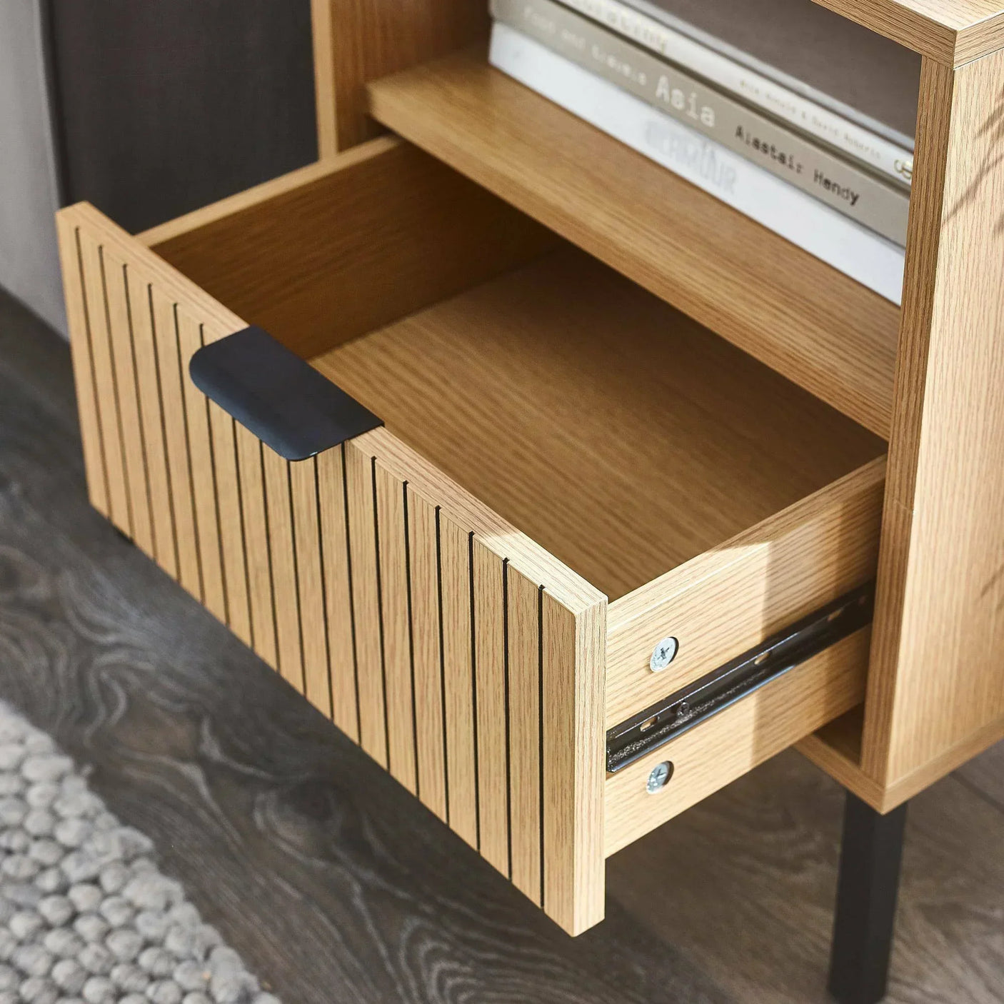 Wooden storage cabinet with open slatted drawer and books on shelf above