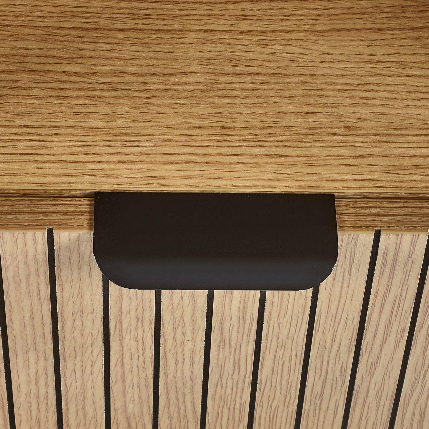 Close view of wooden furniture handle with black metal pull and vertical grooves