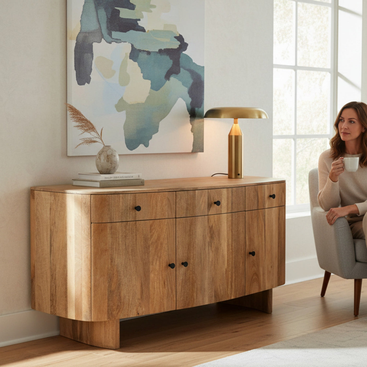 Woman sitting in a living room with a wooden sideboard and abstract painting on the wall.