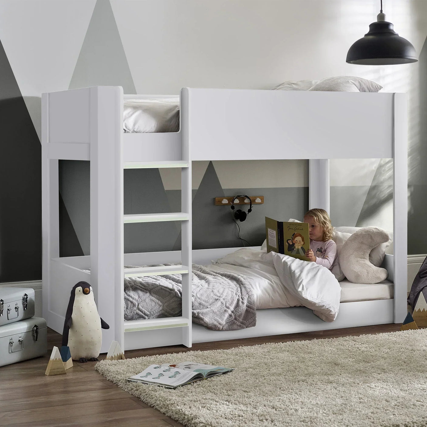 White bunk bed setup in kids room with ladder, child reading on lower bunk, plush penguin nearby