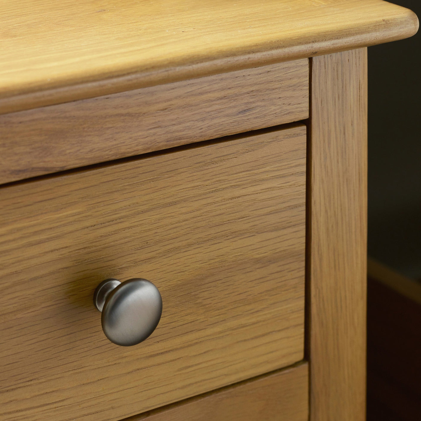 Close up of silver metal knob on light oak bedside table drawer, showing wood grain texture