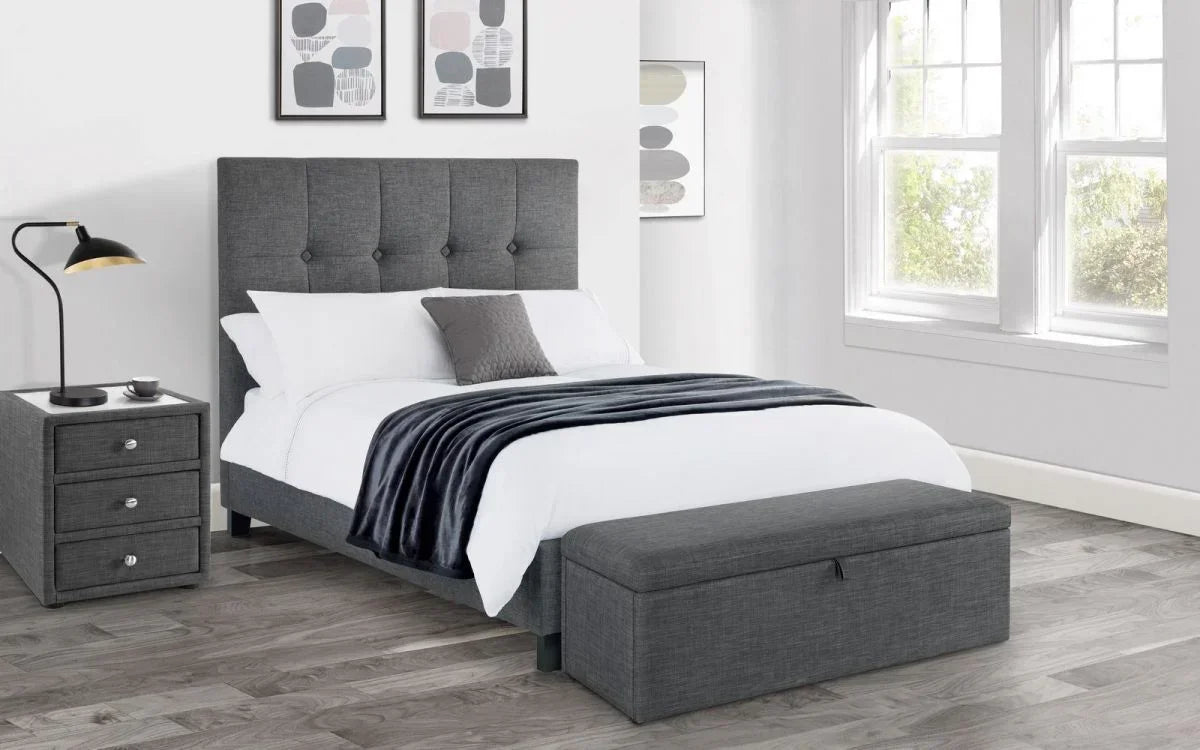 Grey fabric bed with tall buttoned headboard, storage ottoman, and matching bedside table