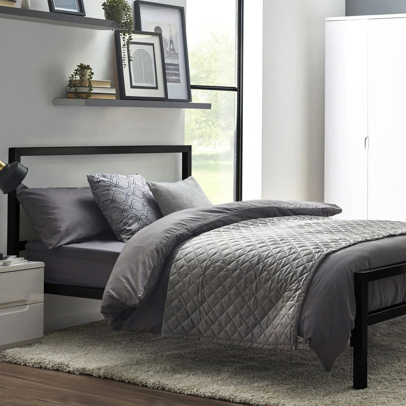 Black metal bed frame with grey bedding in modern bedroom with shelves and wardrobe