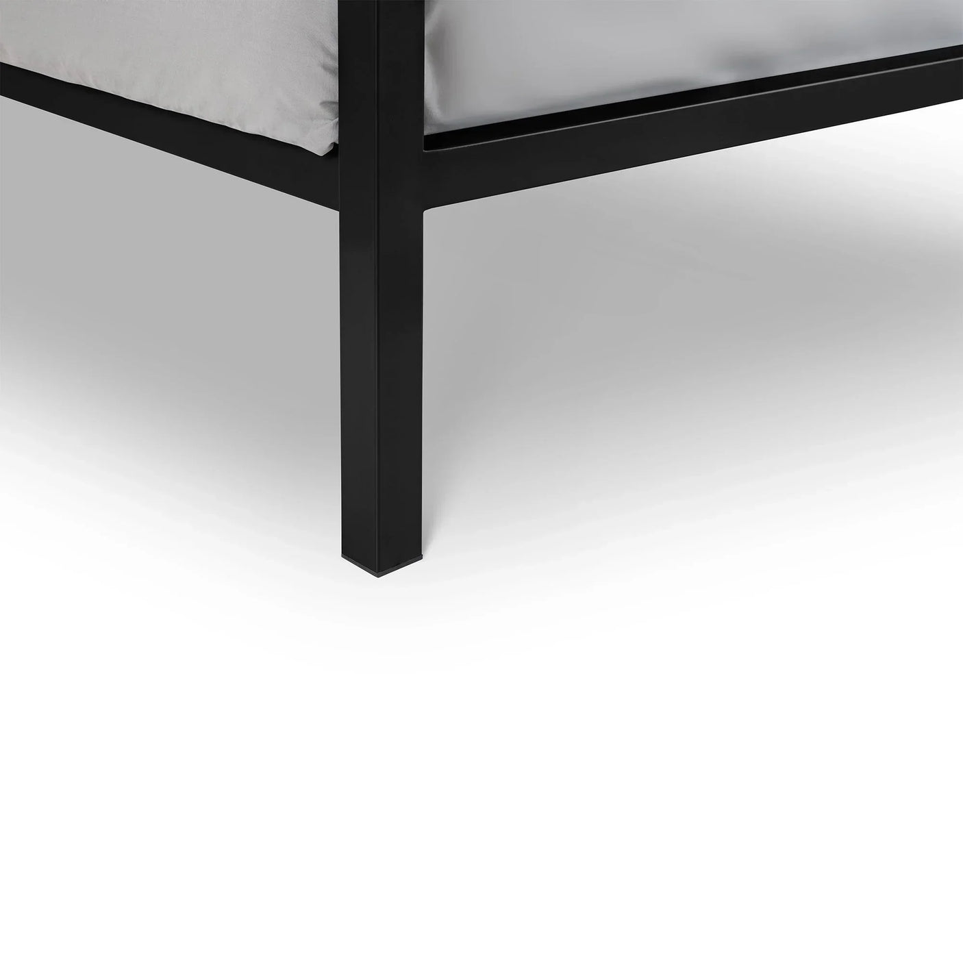 Closeup of black metal bed frame leg with grey mattress above white floor