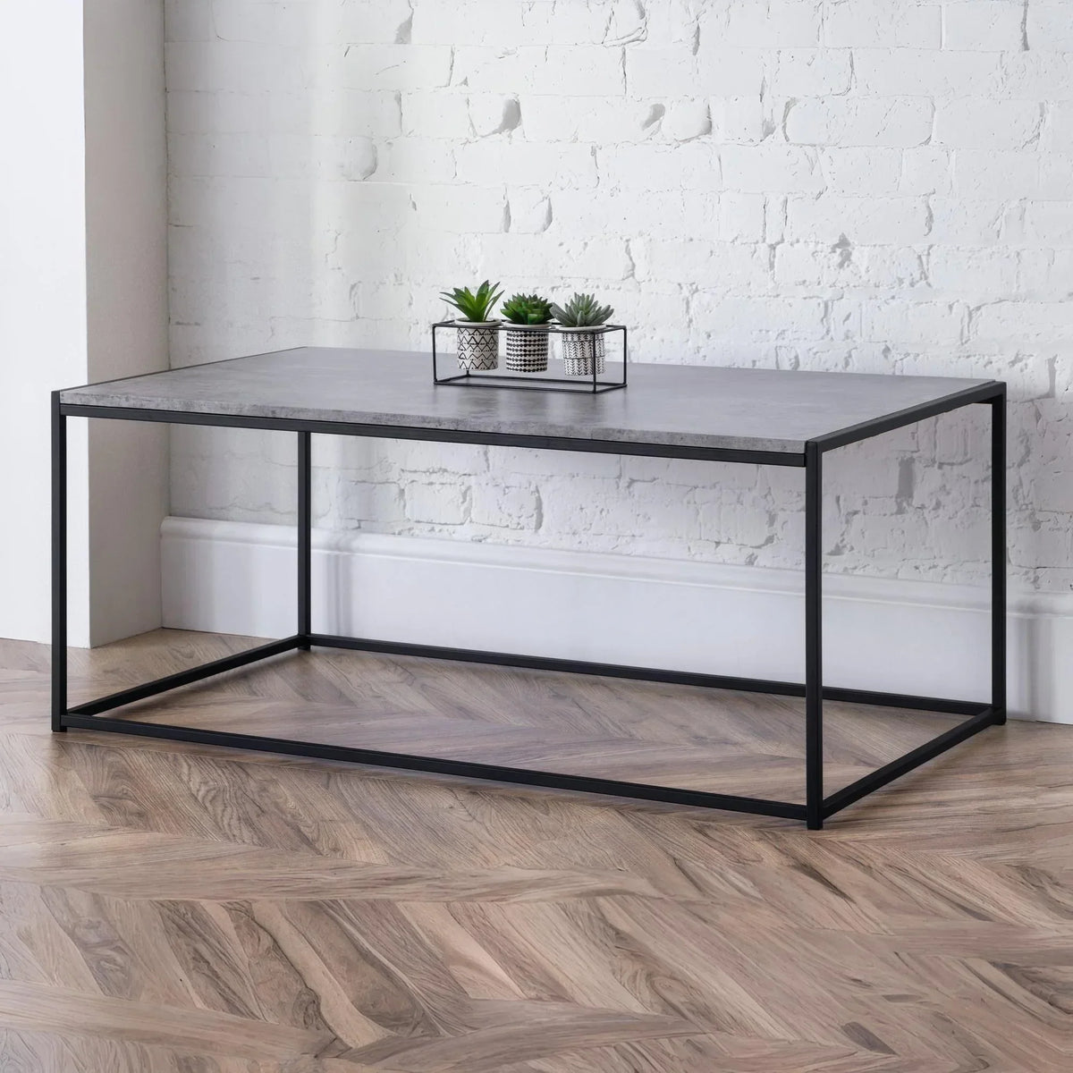 Rectangular coffee table with concrete top and black metal frame on herringbone wood floor