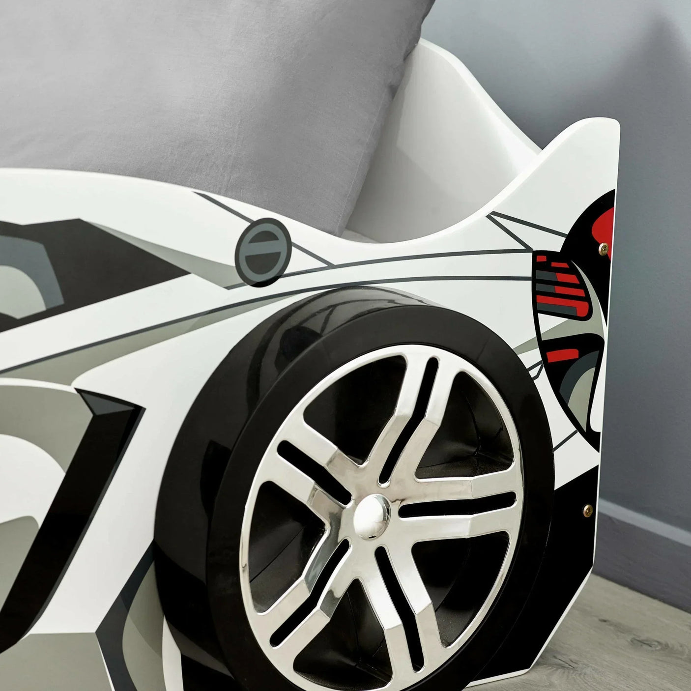 Close-up of children's car bed frame with black alloy wheel design and grey pillow