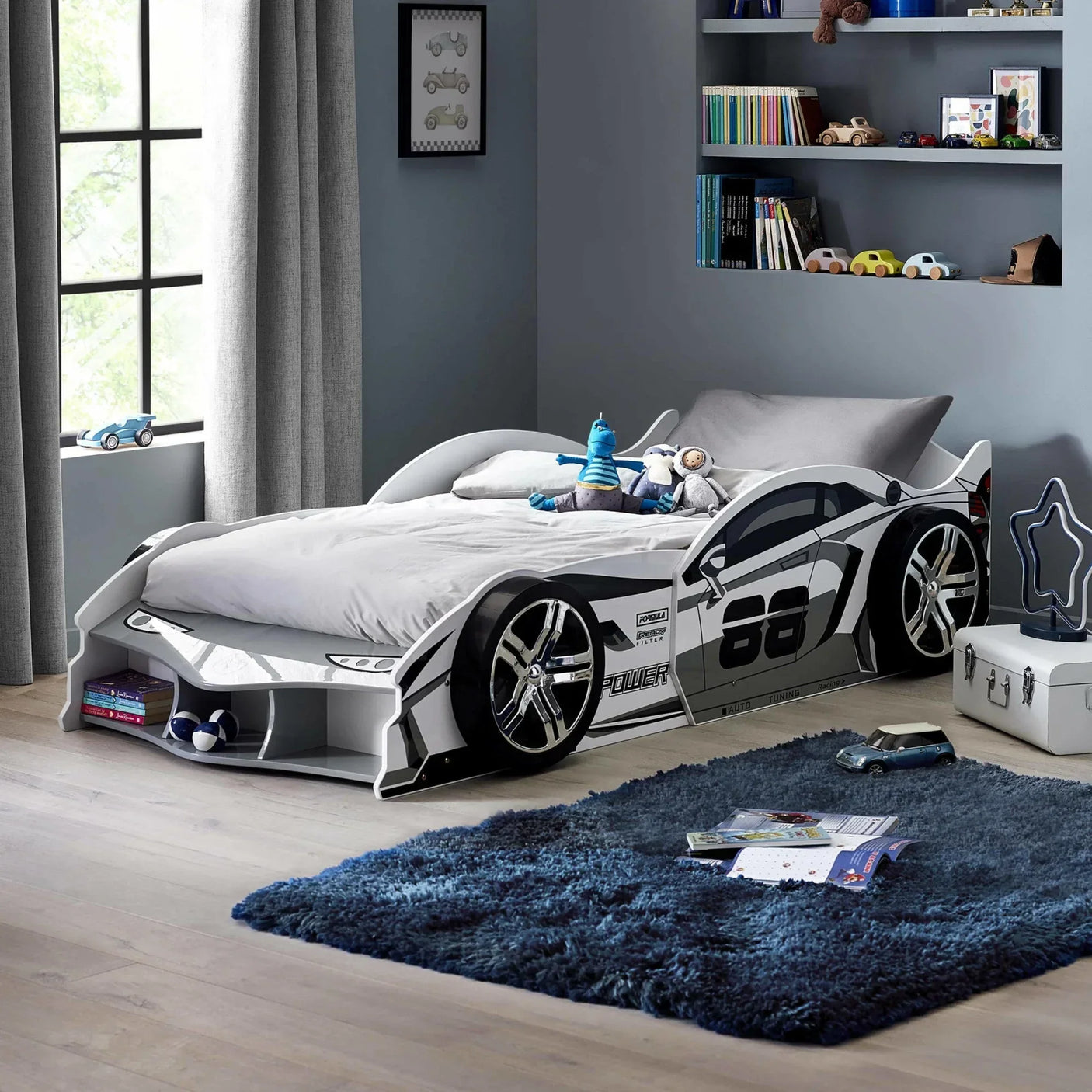White kids car bed with racing design in modern bedroom with blue rug and toy storage