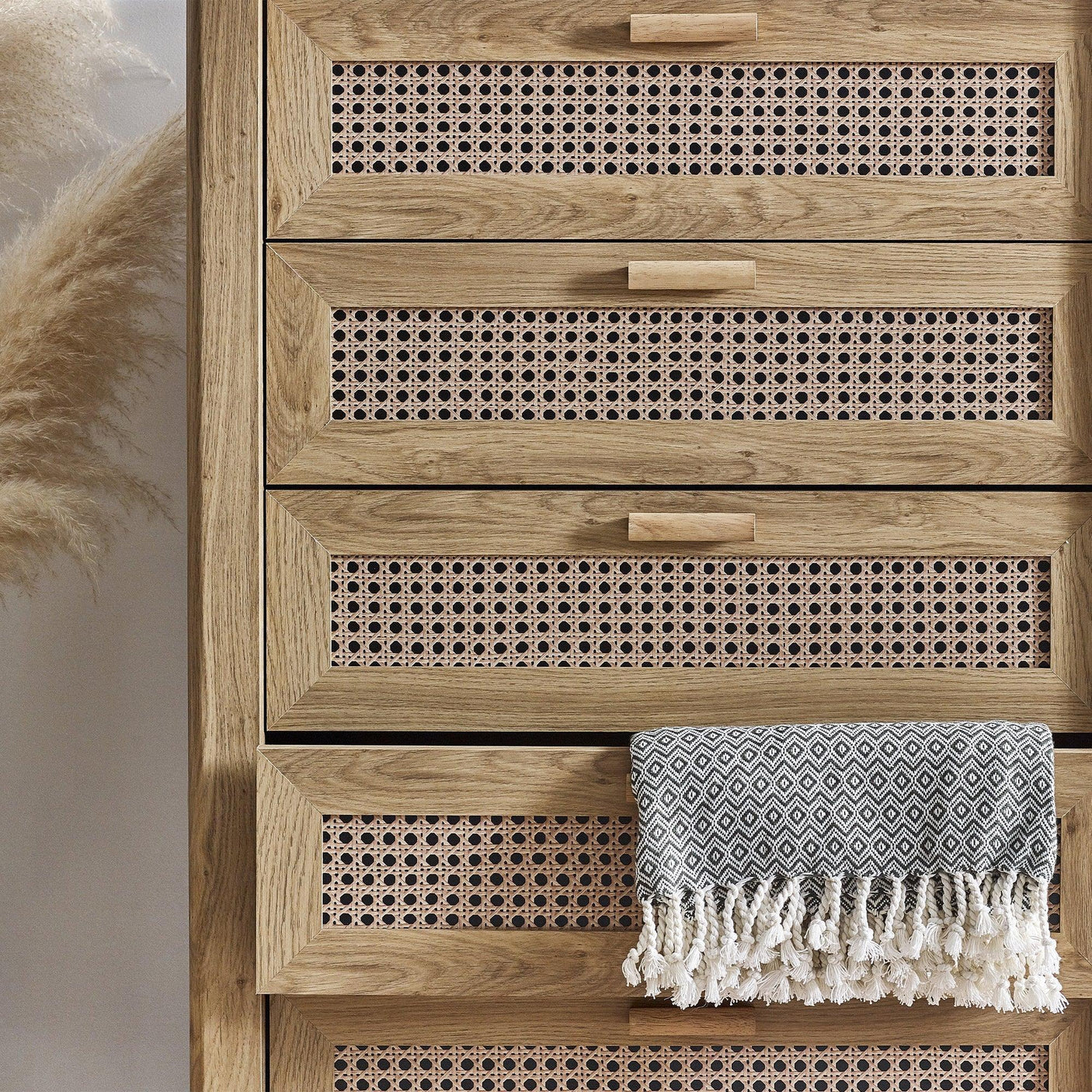 Rattan effect 5 drawer chest with wooden frame and geometric throw draped on lower drawer