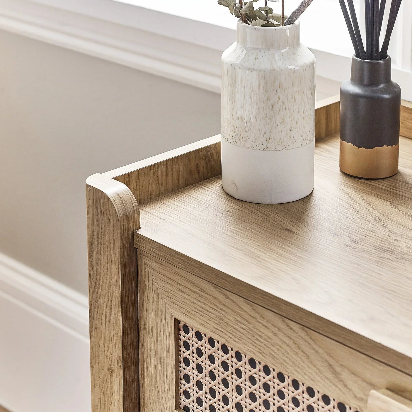 Close-up of rattan effect 5 drawer chest with wood top and decorative vases