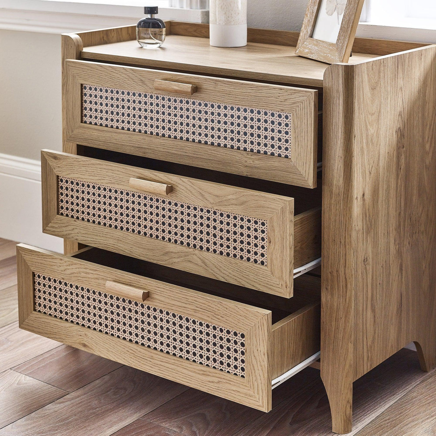 Rattan effect 3 drawer chest with open drawers in a bright room on wood flooring