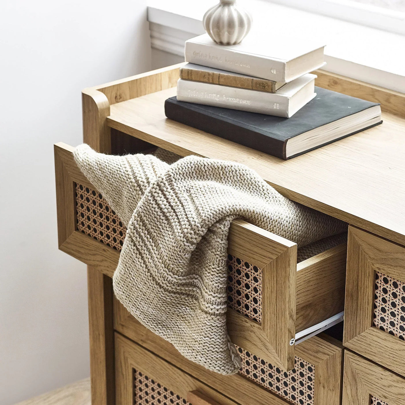 Sydney rattan effect 6 drawer wide chest with open drawer, knit throw, and stacked books