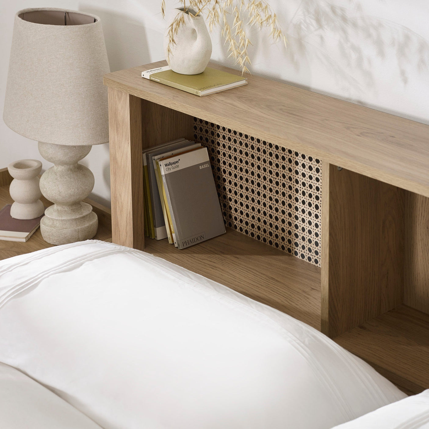 Close-up of oak headboard shelving with books, lamp and decorative vase on top