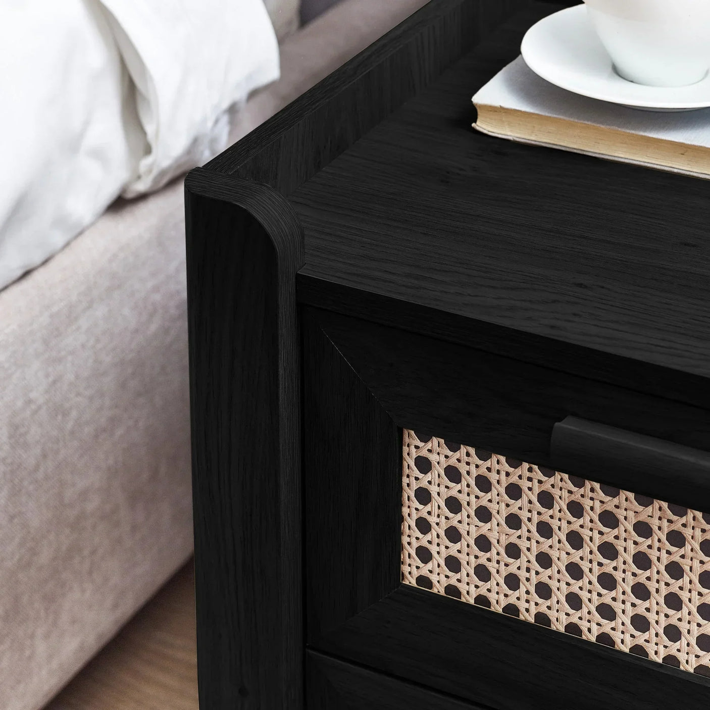 Close-up of black rattan effect bedside table with two drawers and book on top