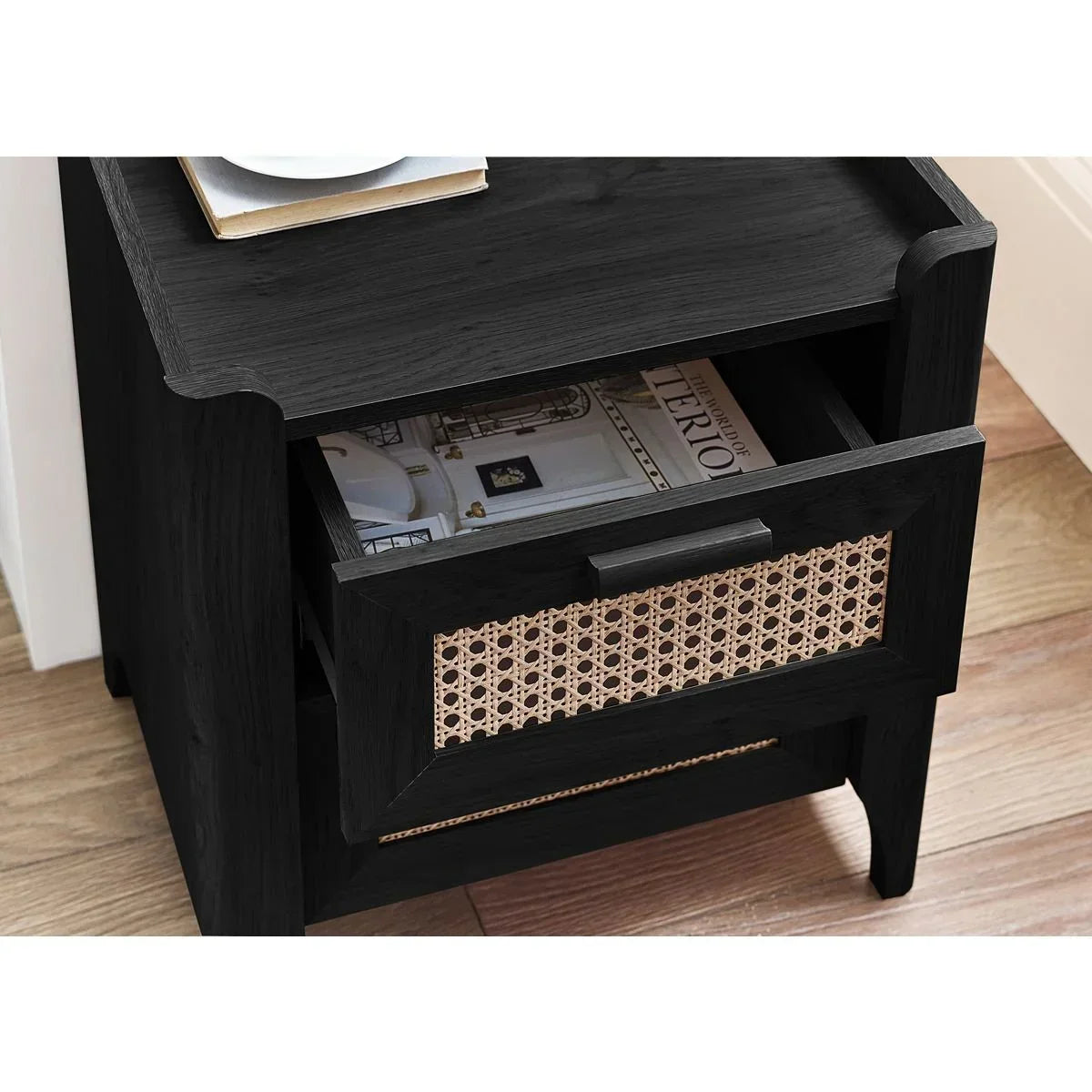 Black wooden bedside table with rattan drawer front and open shelf on wooden floor