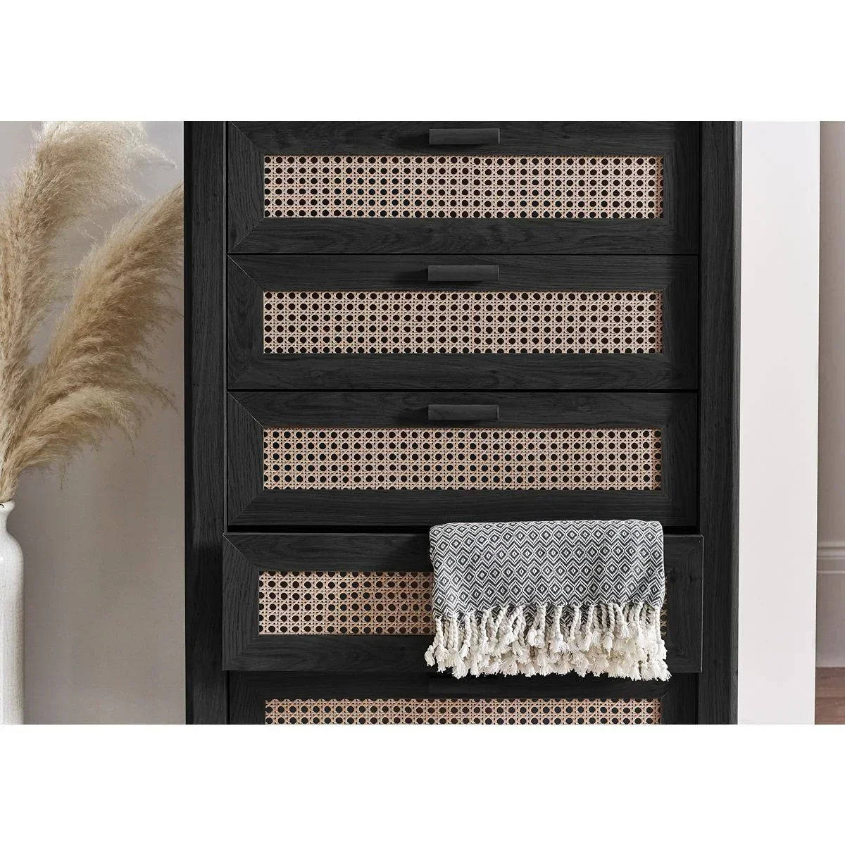 Black wood rattan chest of drawers with woven panel detail and throw in modern interior