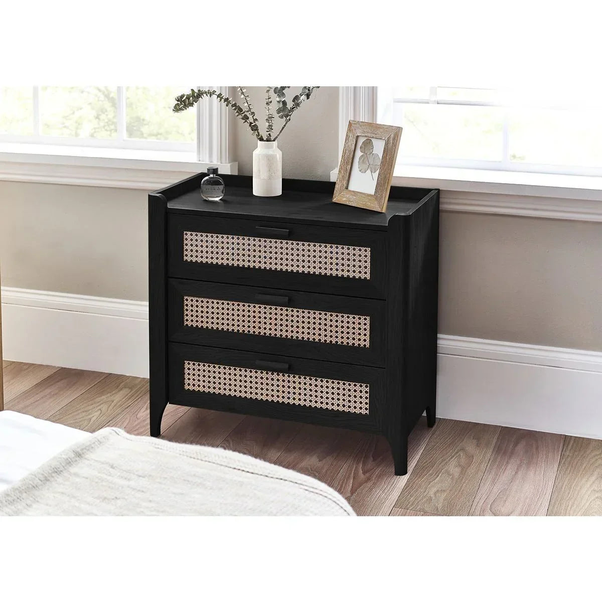 Black wooden chest of drawers with rattan fronts beside window in bedroom