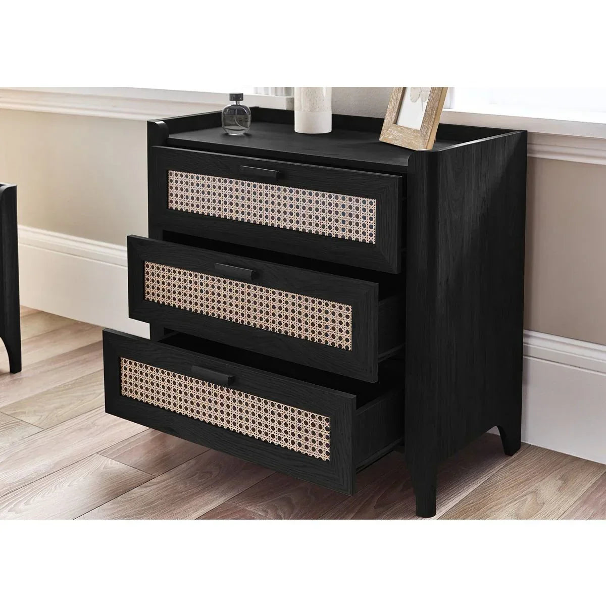 Black wooden chest of drawers with woven rattan fronts in modern bedroom setting