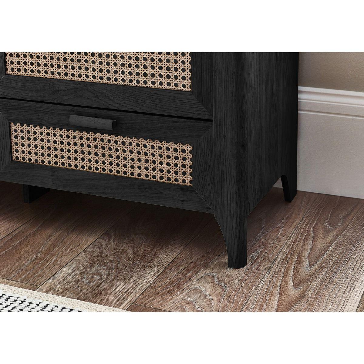 Black wooden bedside table with rattan drawer detail on wood flooring