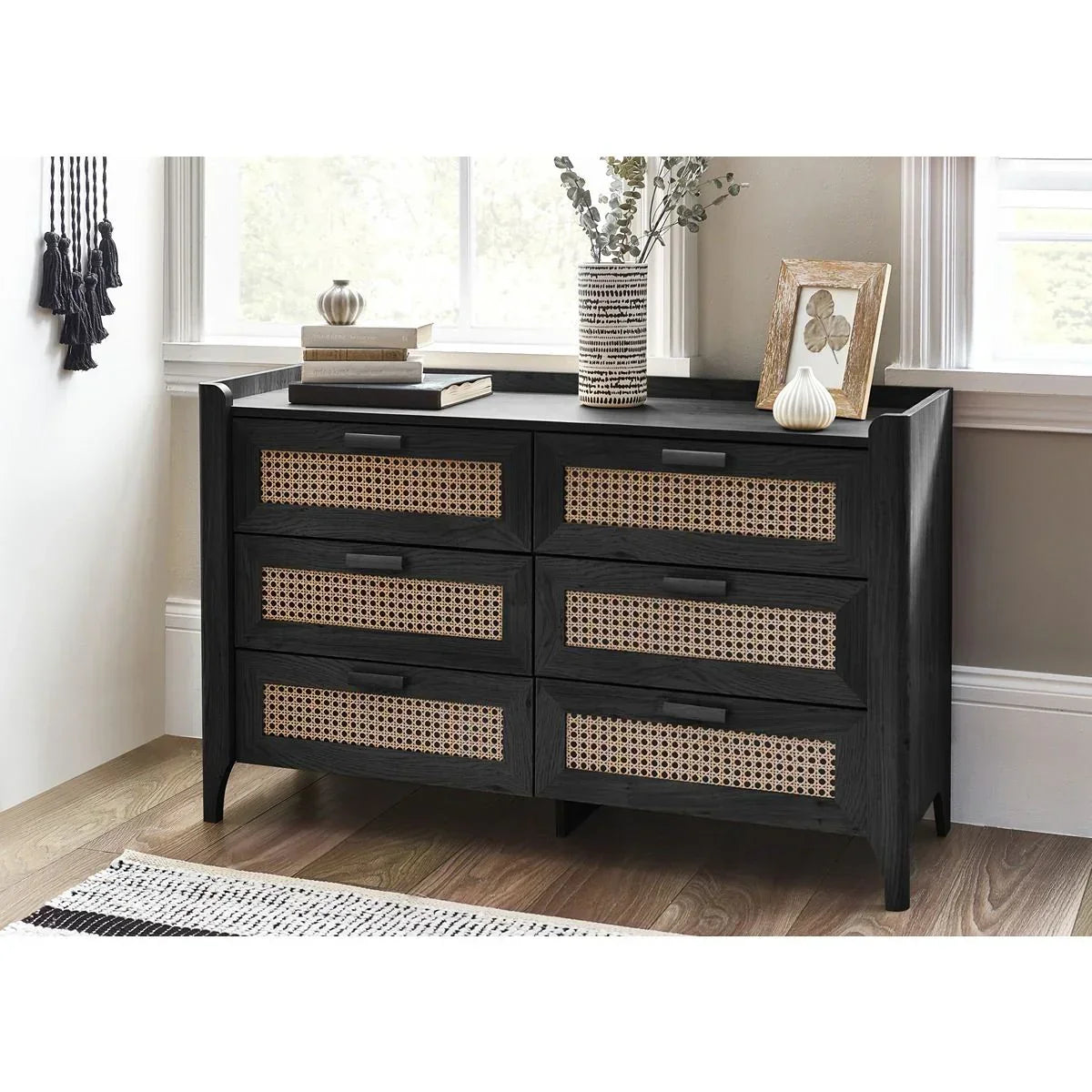 Black wood chest of drawers with rattan fronts in bright bedroom corner