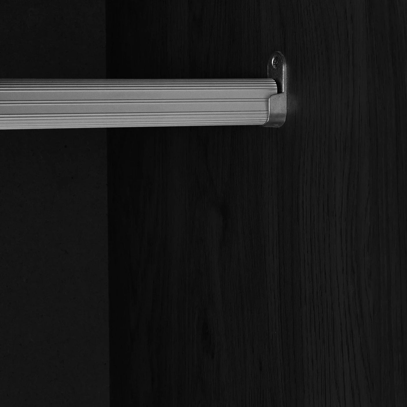 Close-up of wardrobe interior with metal hanging rail and black ash wood finish