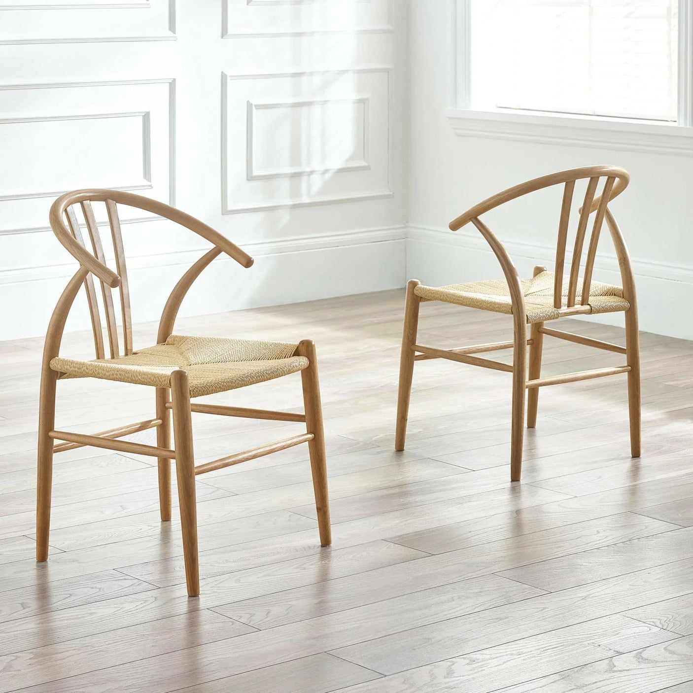 Pair of wooden dining chairs with curved backs and woven seats on light wood flooring