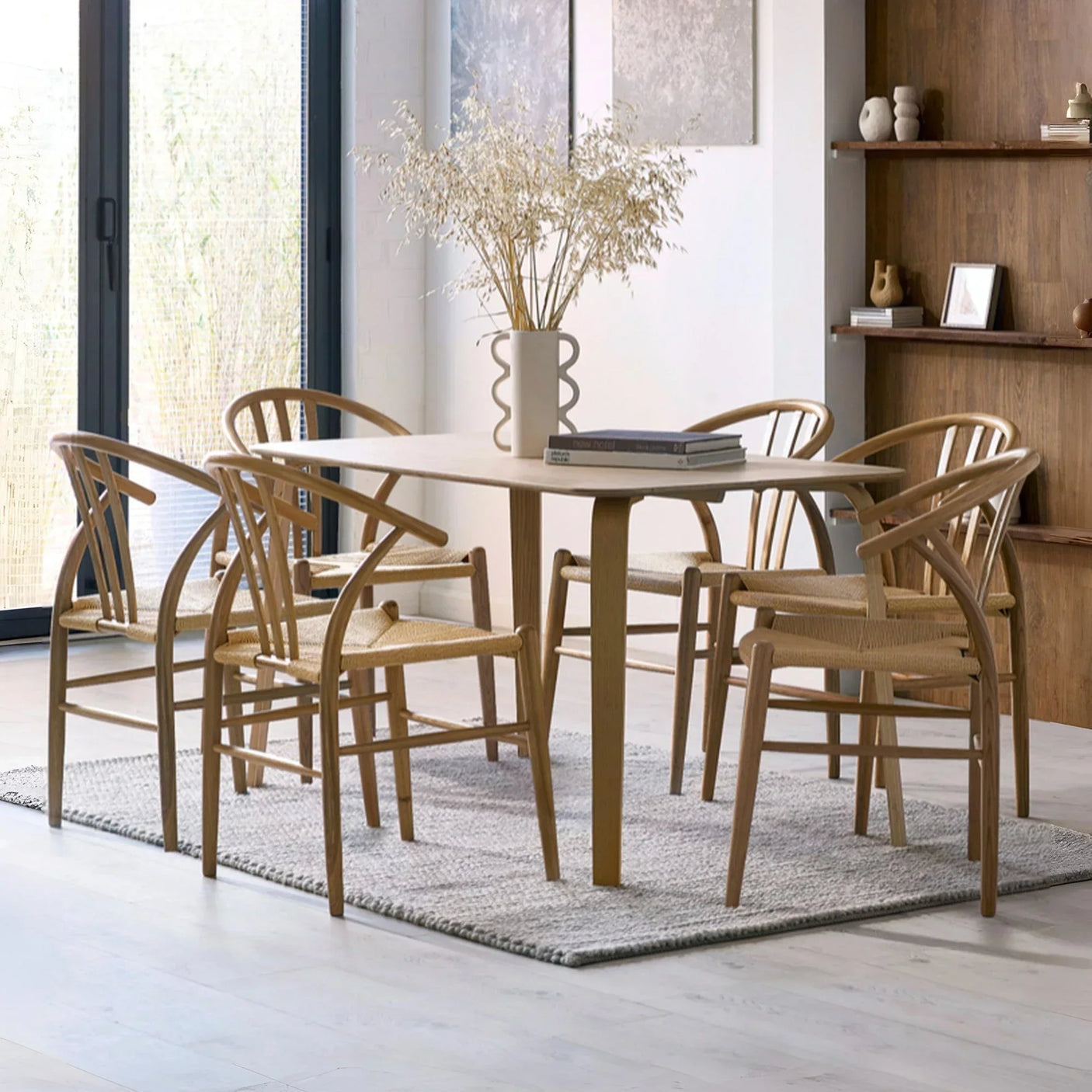 Light wood dining table with six woven seat chairs on grey rug in modern dining room
