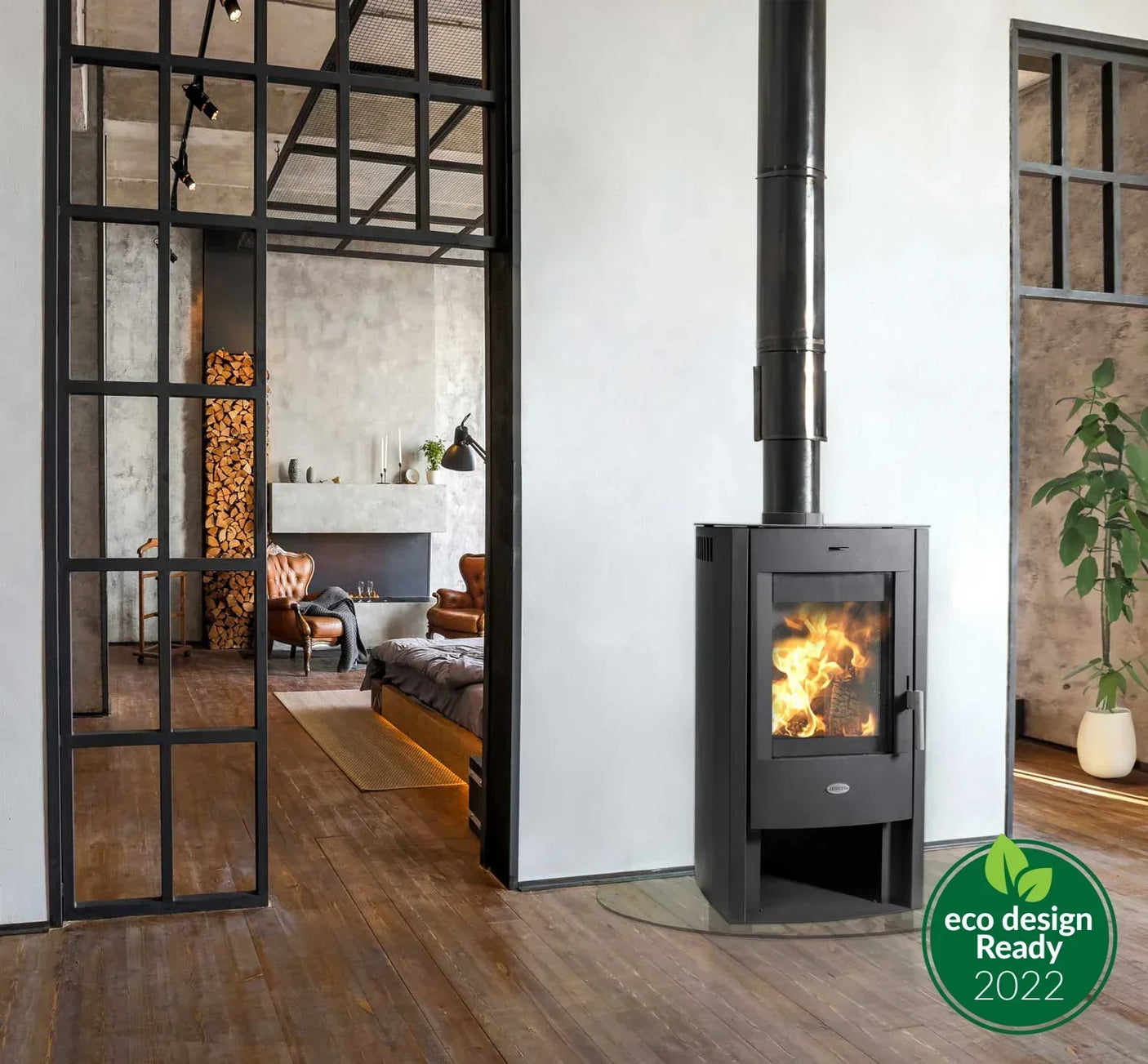 Modern wood burning stove in open plan living space with glass partition and armchairs